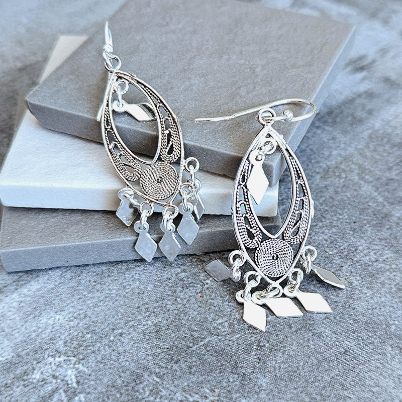 Silver earrings with intricate designs on a stone surface