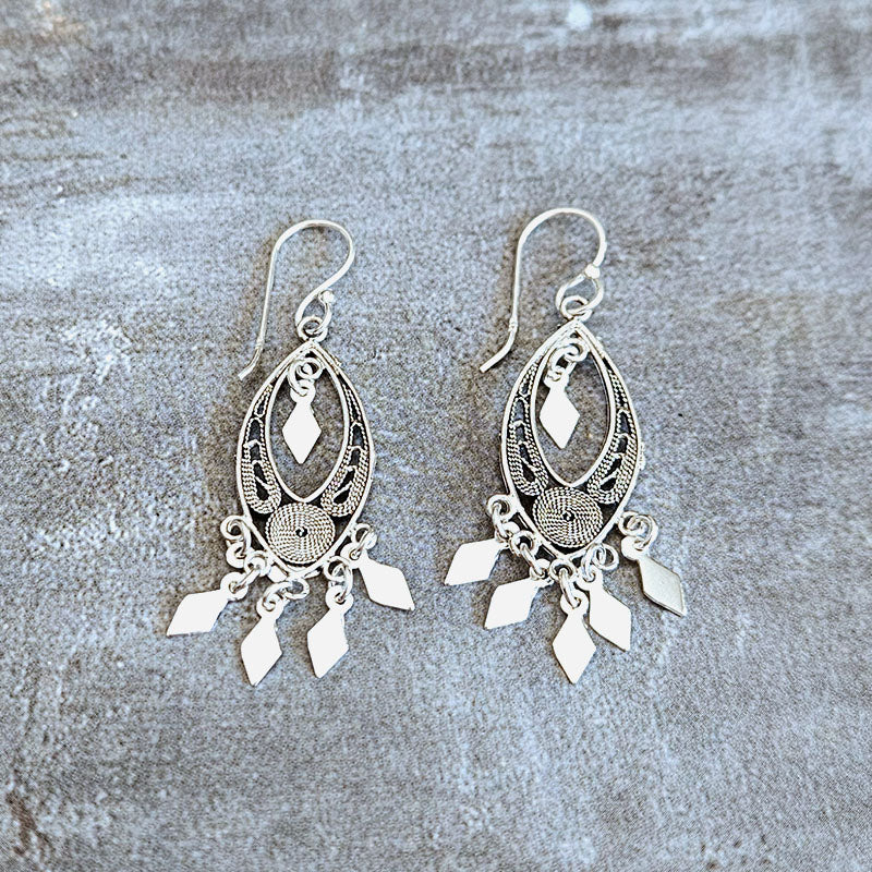 Pair of silver earrings with intricate designs on a textured surface