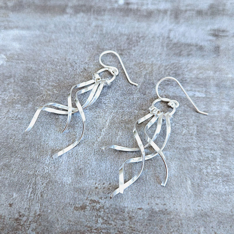 Silver ribbon-style earrings on a textured gray surface