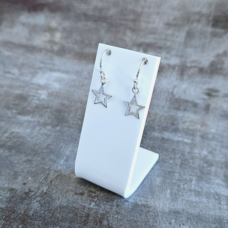 Silver star earrings on a white stand against a gray background