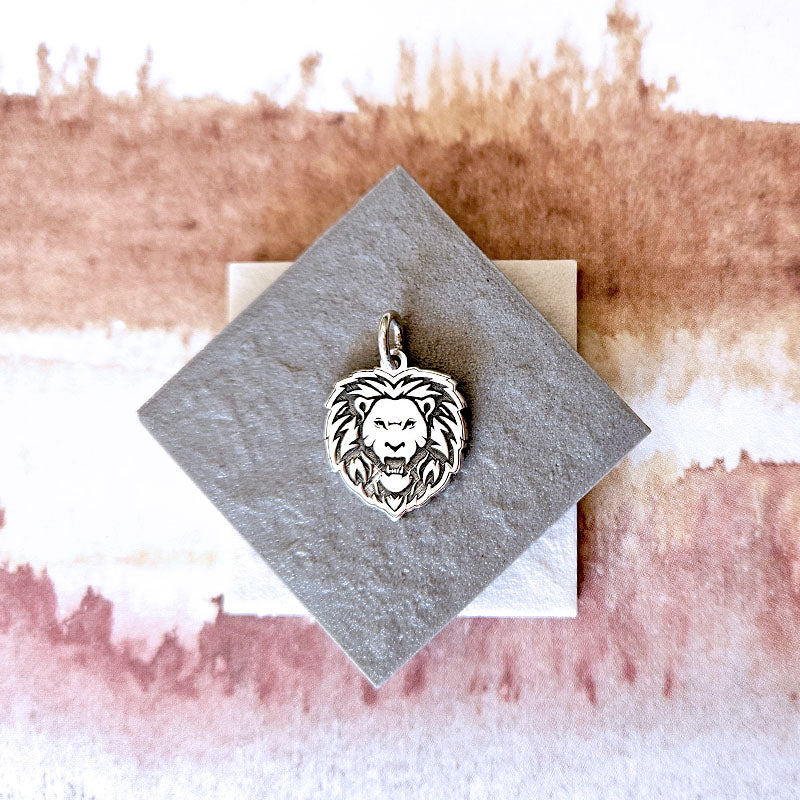 Silver lion head pendant on a textured card with a watercolor background