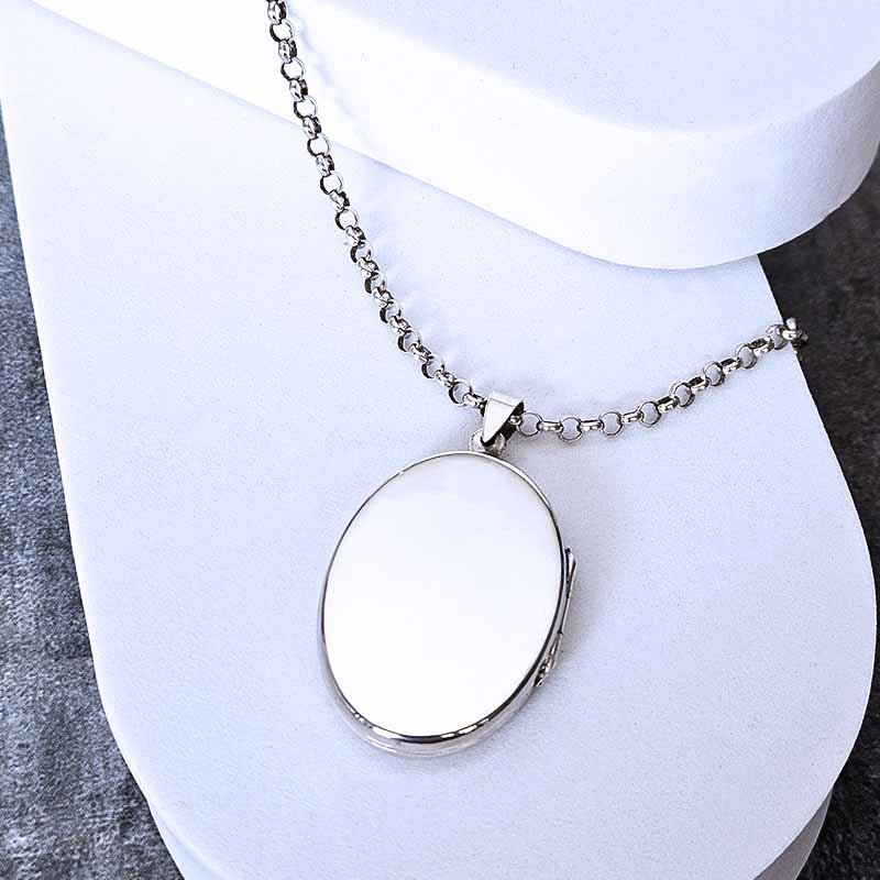 Silver locket necklace on a white stand with a gray surface underneath