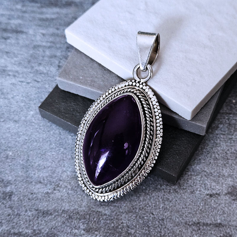 Silver pendant with a purple gemstone on a textured surface