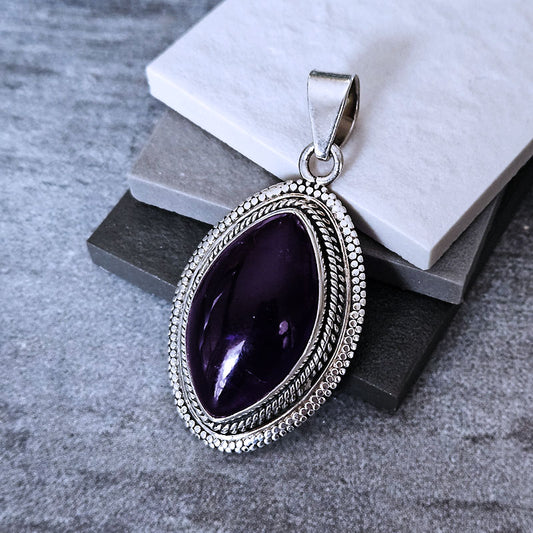 Silver pendant with a purple gemstone on a textured surface