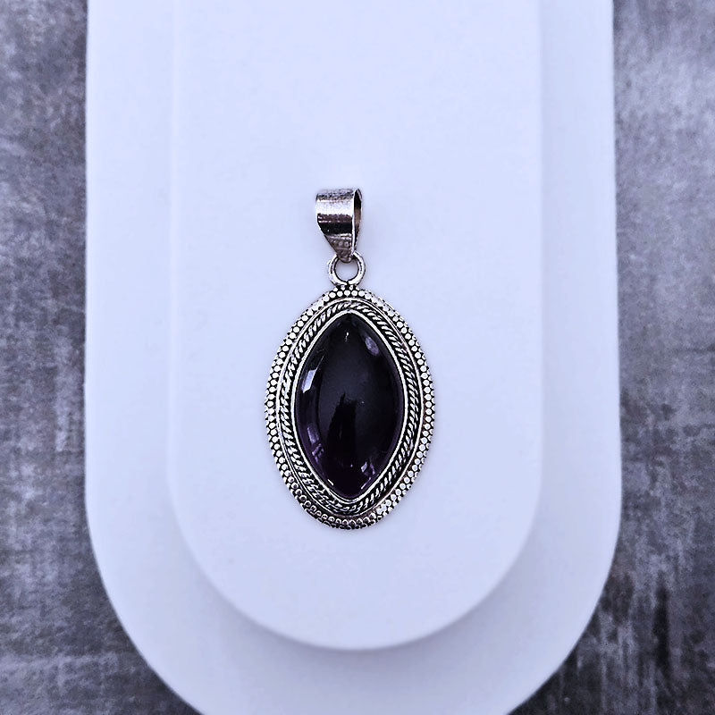 Silver pendant with a purple stone on a white stand against a gray background
