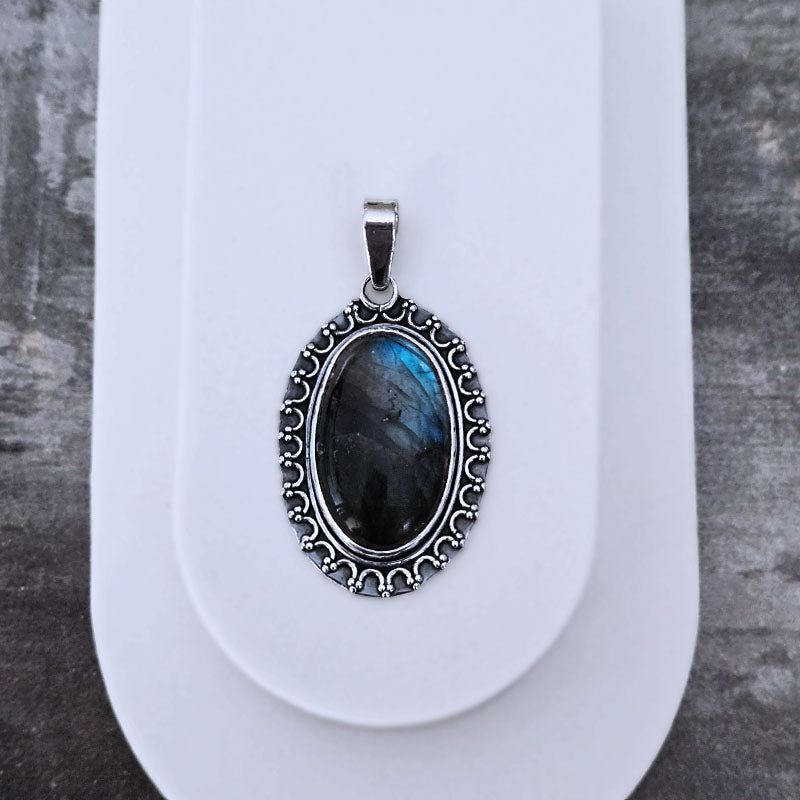 Silver pendant with a blue stone on a white stand against a gray background