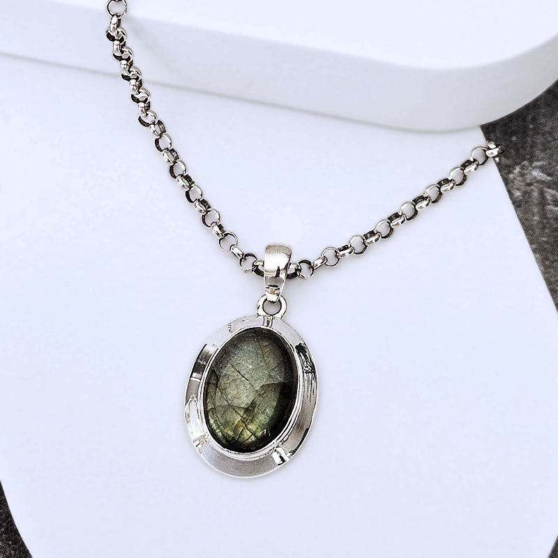 A silver chain necklace with an oval pendant featuring a greenish iridescent stone, displayed on a white surface.