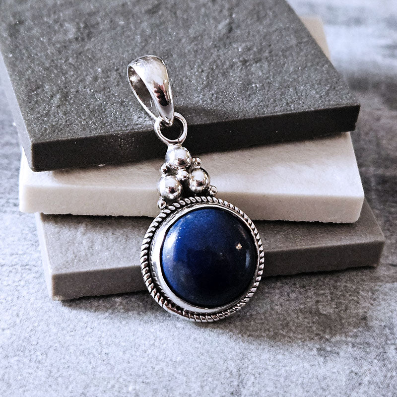Silver pendant with a blue stone on a textured surface