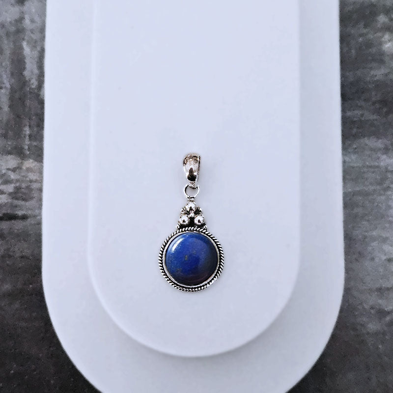 Blue stone pendant with silver frame on a white stand against a gray background