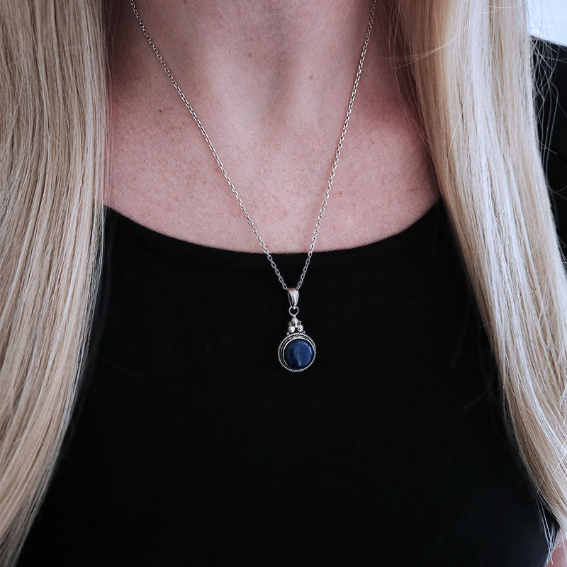 Necklace with a blue pendant worn by a person with blonde hair.