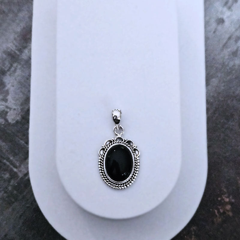 Black stone pendant with silver frame on a white oval stand against a marble background