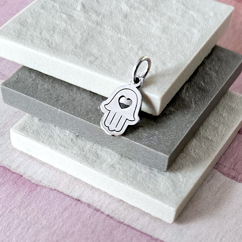 Silver Hamsa hand pendant on a textured stone surface