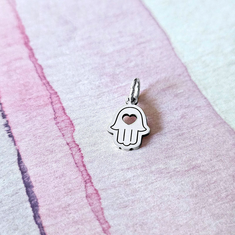 Silver Hamsa hand charm on a pink and white fabric background