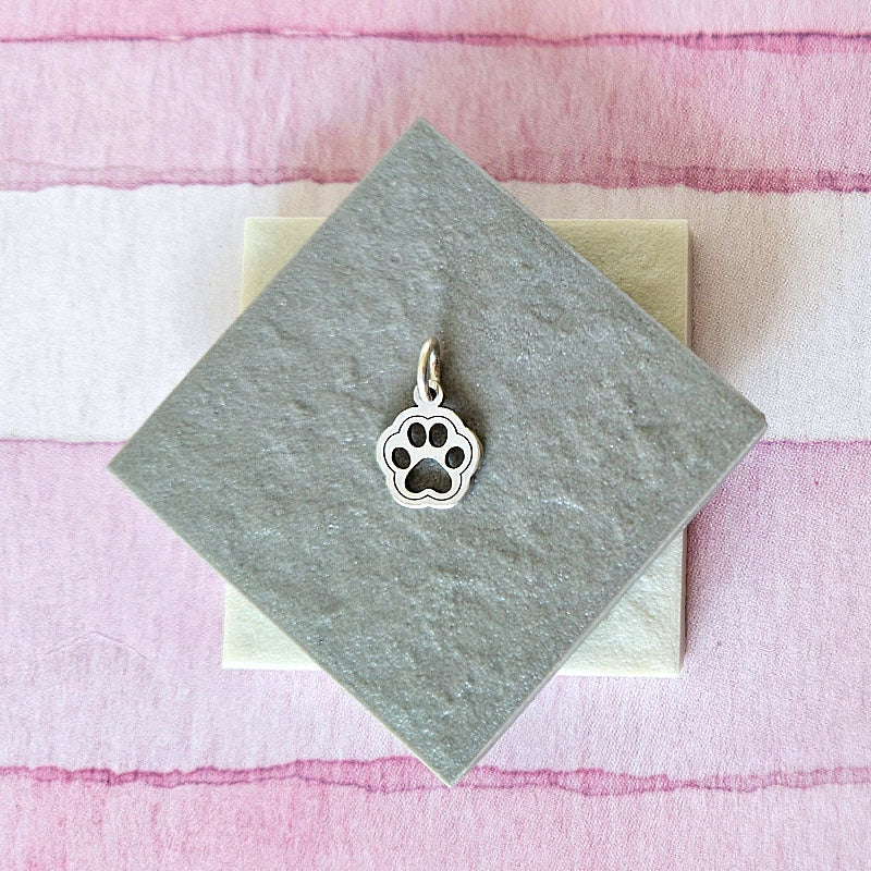 Silver paw print charm on a gray card with a pink and white striped background