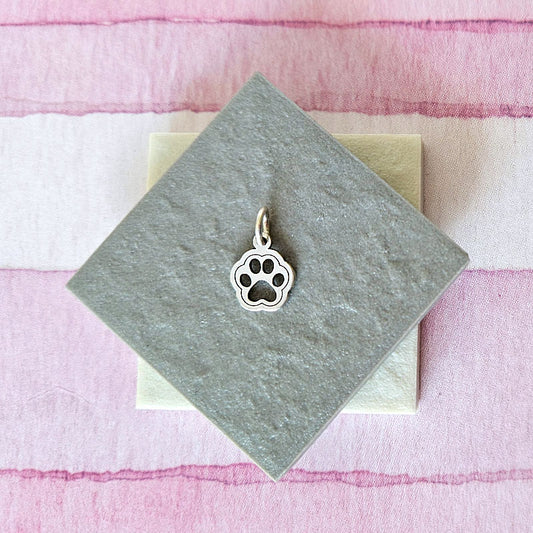 Silver paw print charm on a gray card with a pink and white striped background
