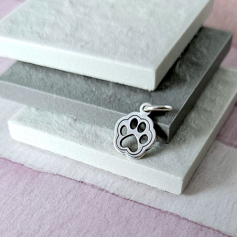 Silver paw print charm on a textured stone surface