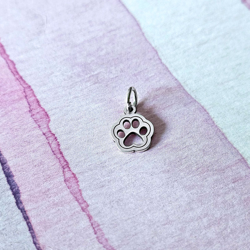 Silver paw print charm on a textured pink and purple fabric background