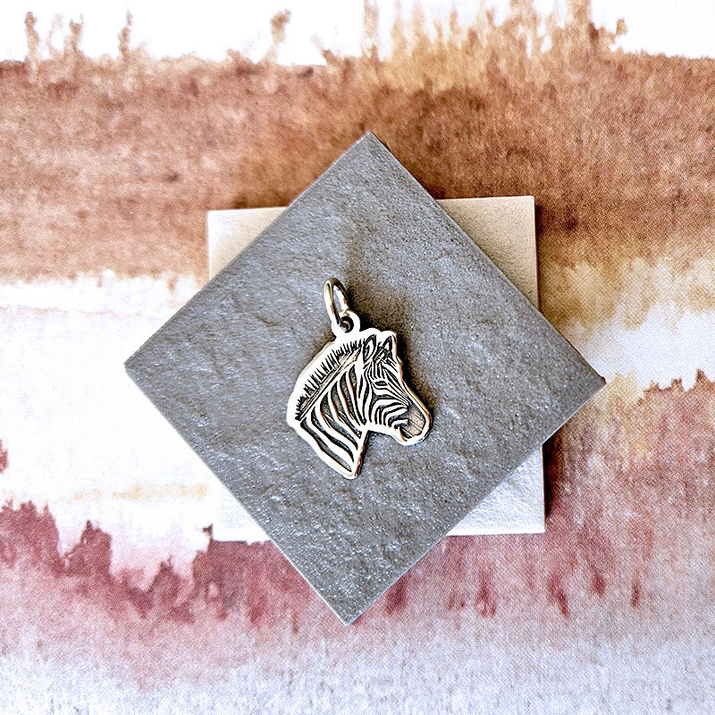 Silver zebra head pendant on a textured card with a watercolor background