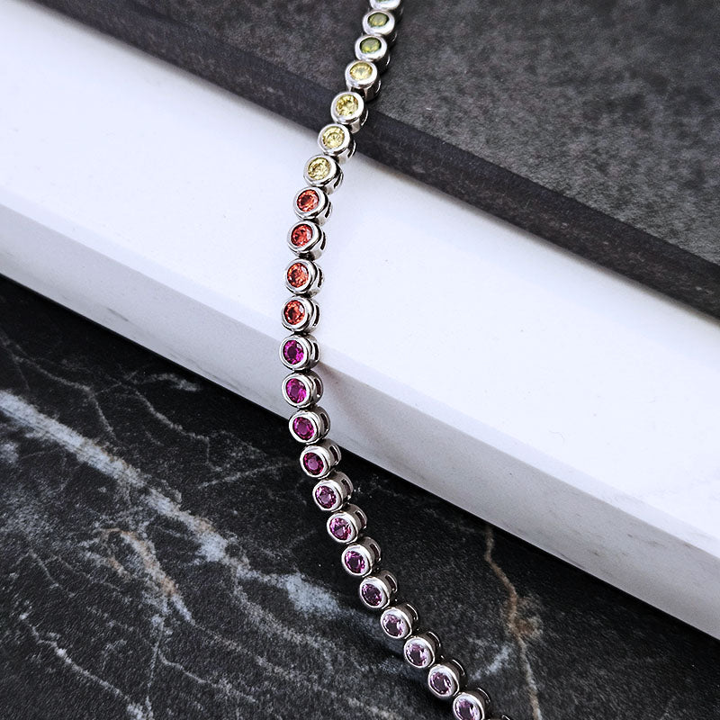 A silver-toned chakra bracelet with multiple colorful gemstones, draped diagonally across a white book on a dark marble surface.