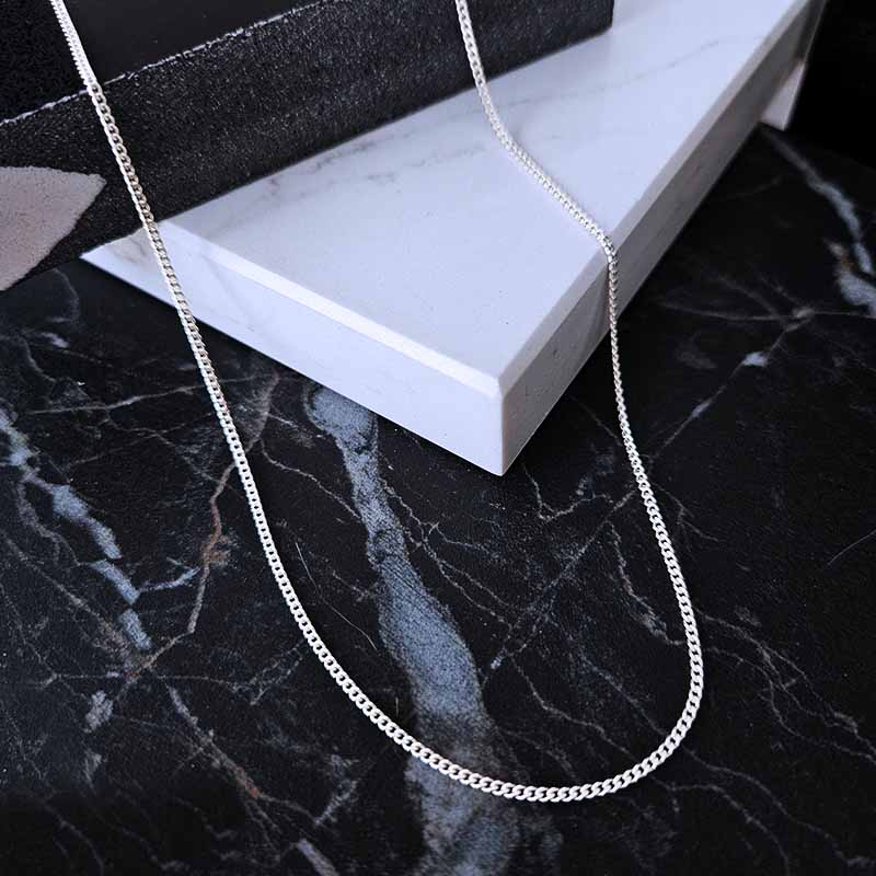 Sterling Silver curb chain - 1,2mm thickness on a black marble surface
