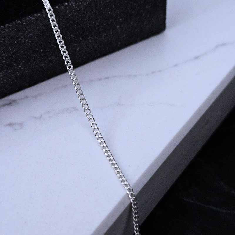 Close up view of a Sterling Silver curb chain on a white marble surface
