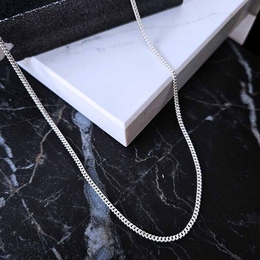 A sterling silver curb link chain on a black and white marble surface
