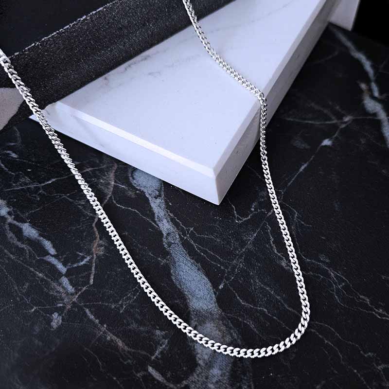 Sterling Silver Curb Chain scattered on a black and white shiny marble surface
