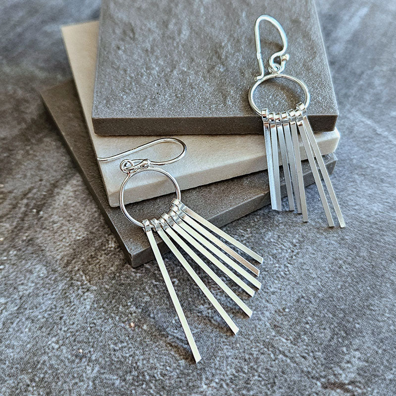 Silver fringe earrings on a textured surface with a neutral background