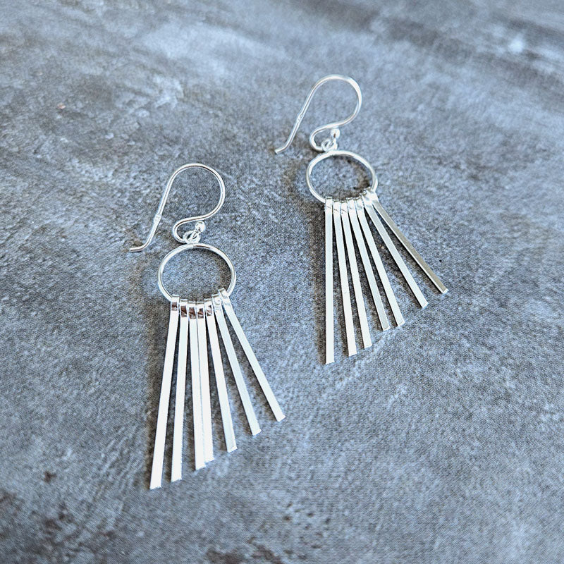 Silver fringe earrings on a textured gray surface