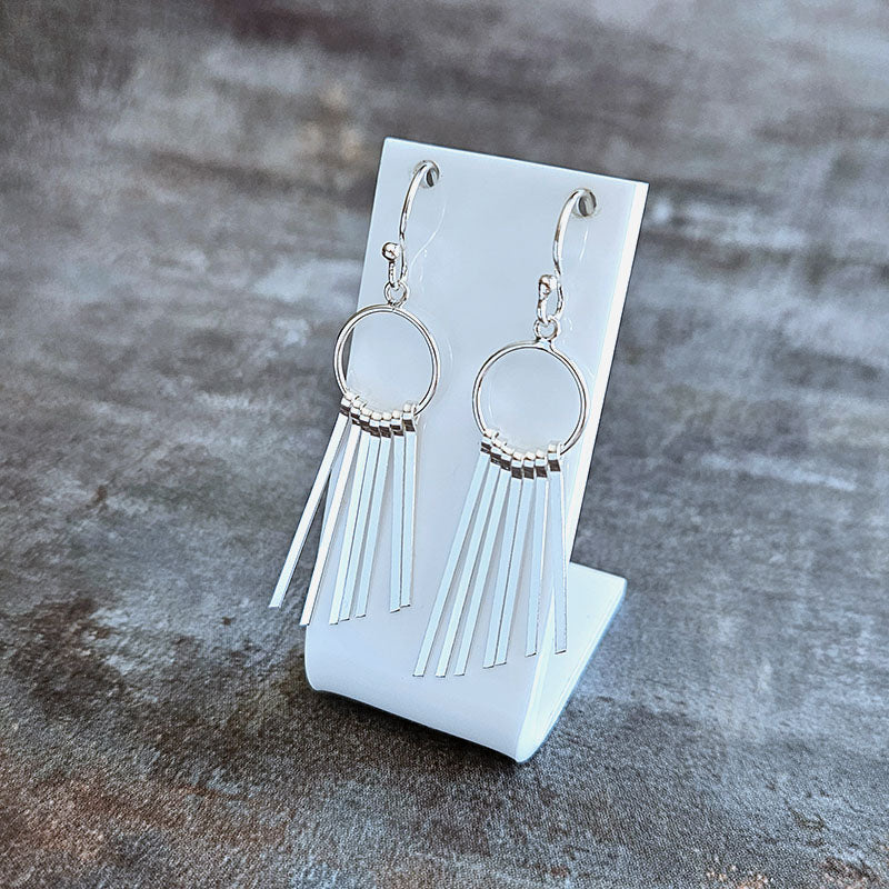 Silver fringe earrings on a white card against a textured gray background