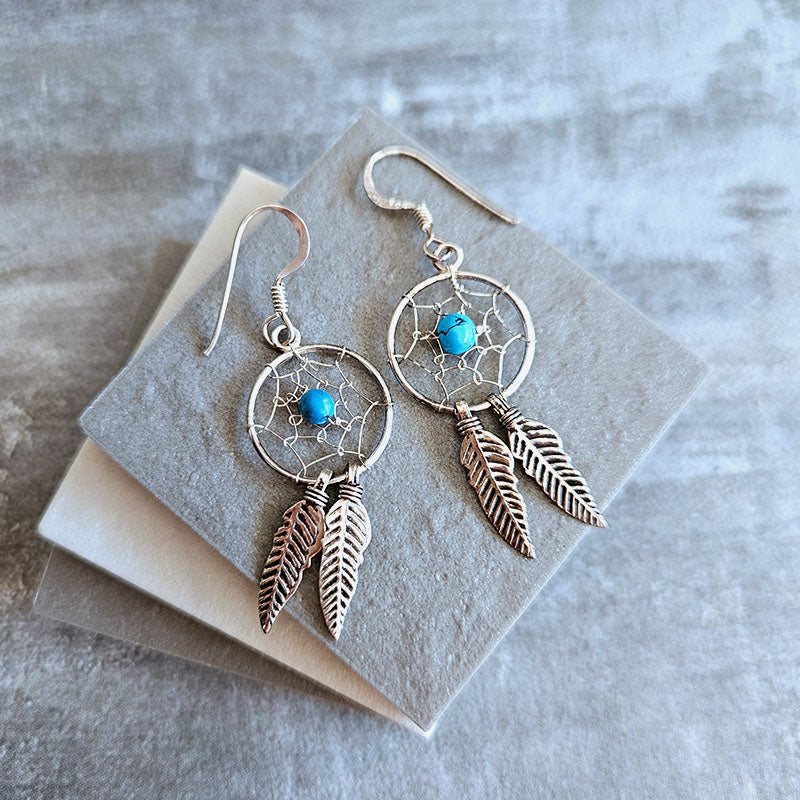 Silver dreamcatcher earrings with turquoise stones and feathers on a gray surface