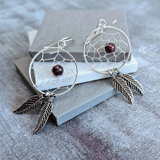 Silver dreamcatcher earrings with feathers and beads on a gray surface