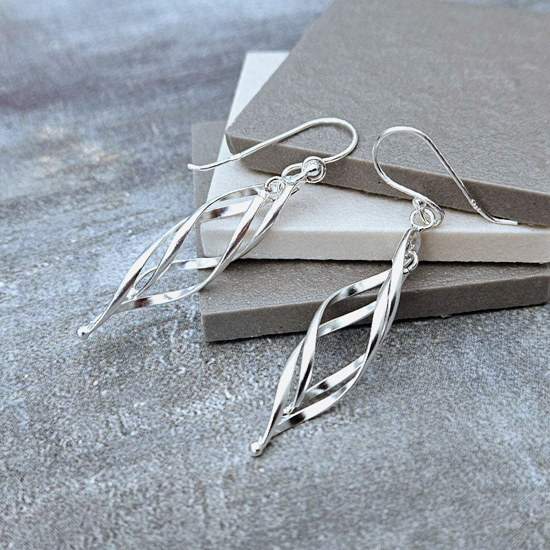 Silver leaf-shaped earrings on a textured surface