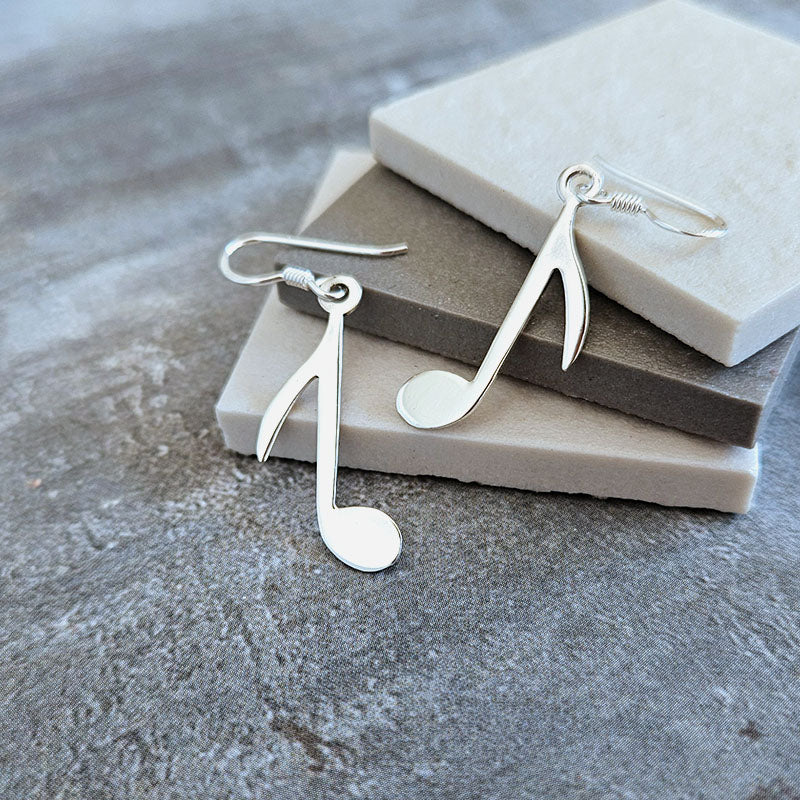 Silver music note earrings on a stone surface