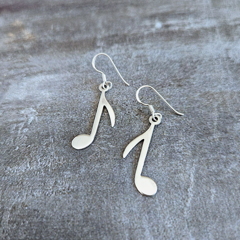 Silver music note earrings on a textured gray surface