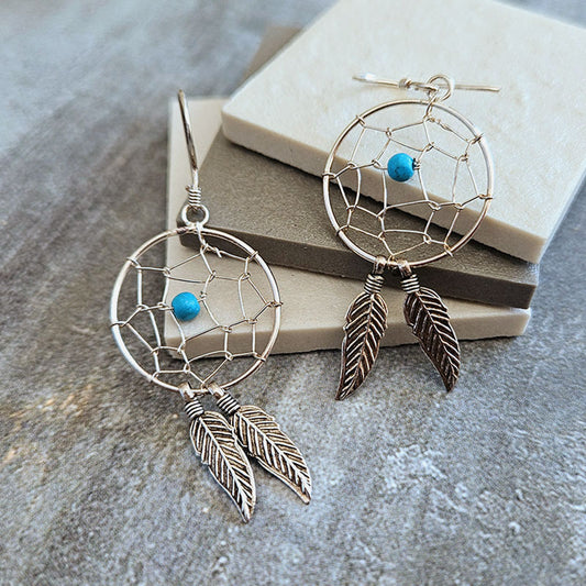 Dreamcatcher earrings with feathers and turquoise stones on a stone surface