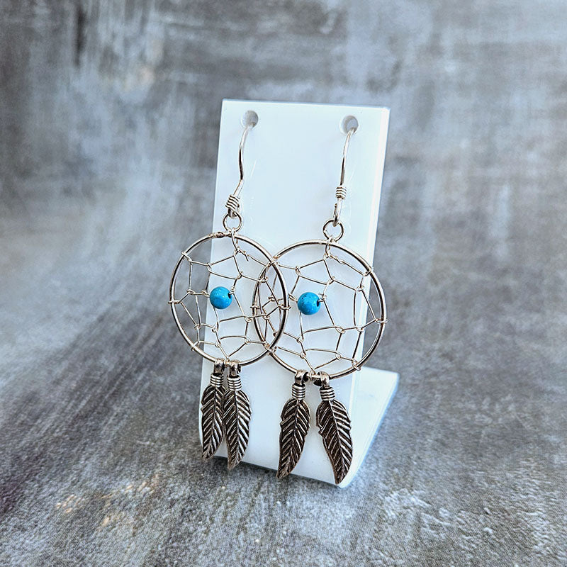 Dreamcatcher earrings with feathers and beads on a gray surface