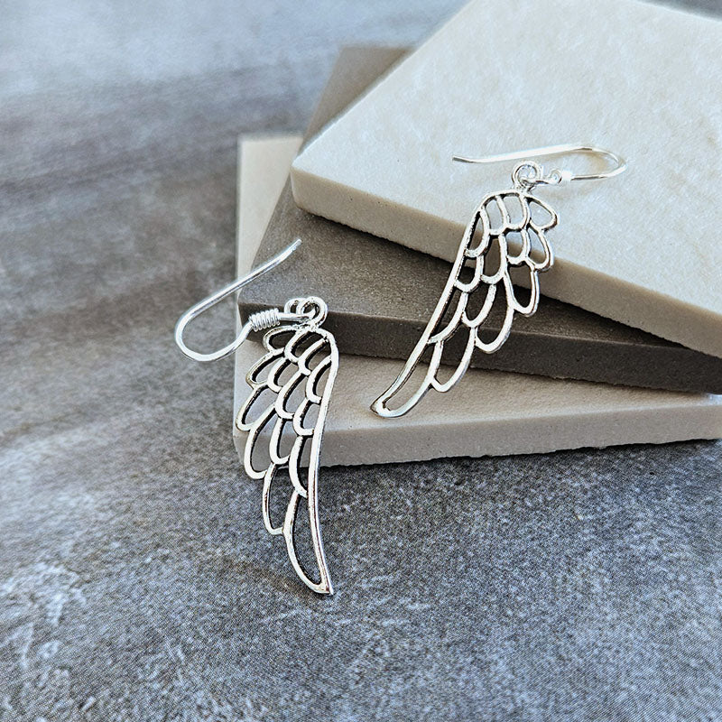 Silver wing-shaped earrings on a stone surface
