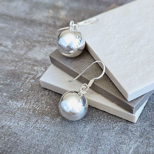 Silver sphere earrings on a textured surface with a book