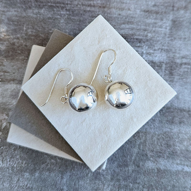 Silver sphere earrings on a gray textured surface with a white card