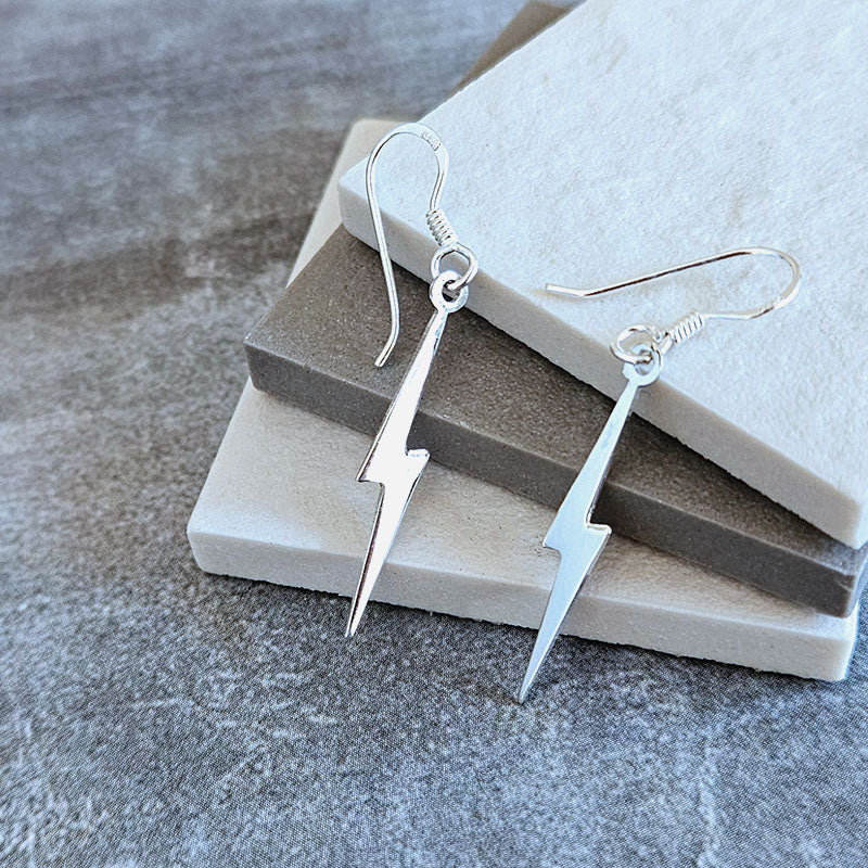 Silver lightning bolt earrings on a stone surface