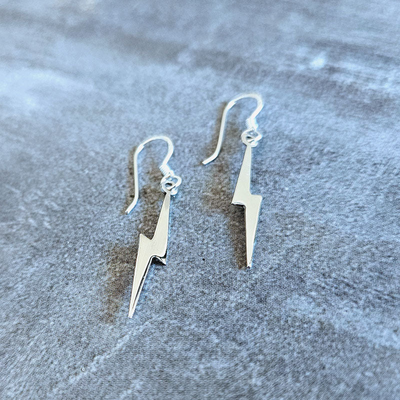 Silver lightning bolt earrings on a textured gray surface