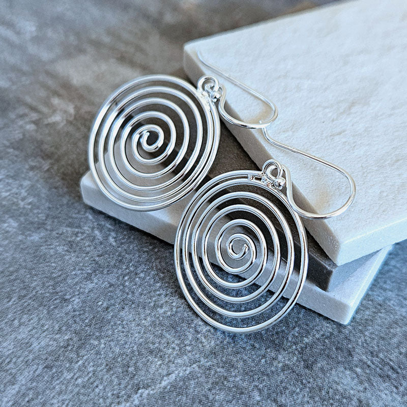 Silver spiral earrings on a gray stone surface