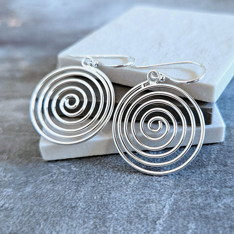 Silver spiral earrings on a gray surface with a white box in the background