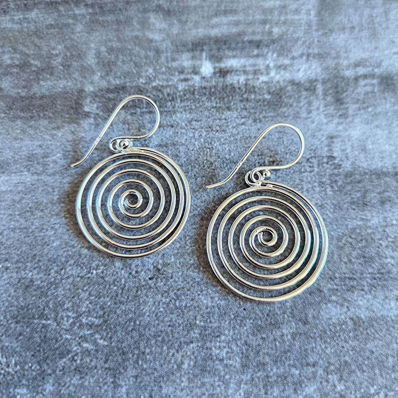 Silver spiral earrings on a textured gray surface