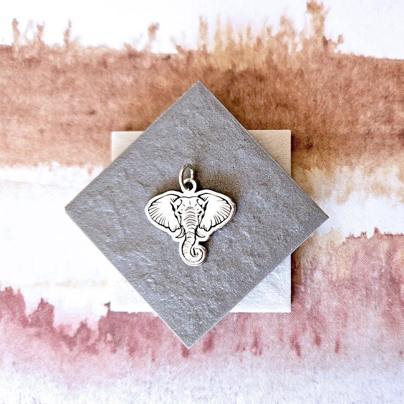 Silver elephant pendant on a textured card with a watercolor background
