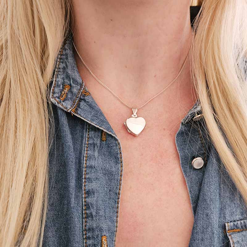 Person wearing a silver heart-shaped pendant necklace with a denim jacket.