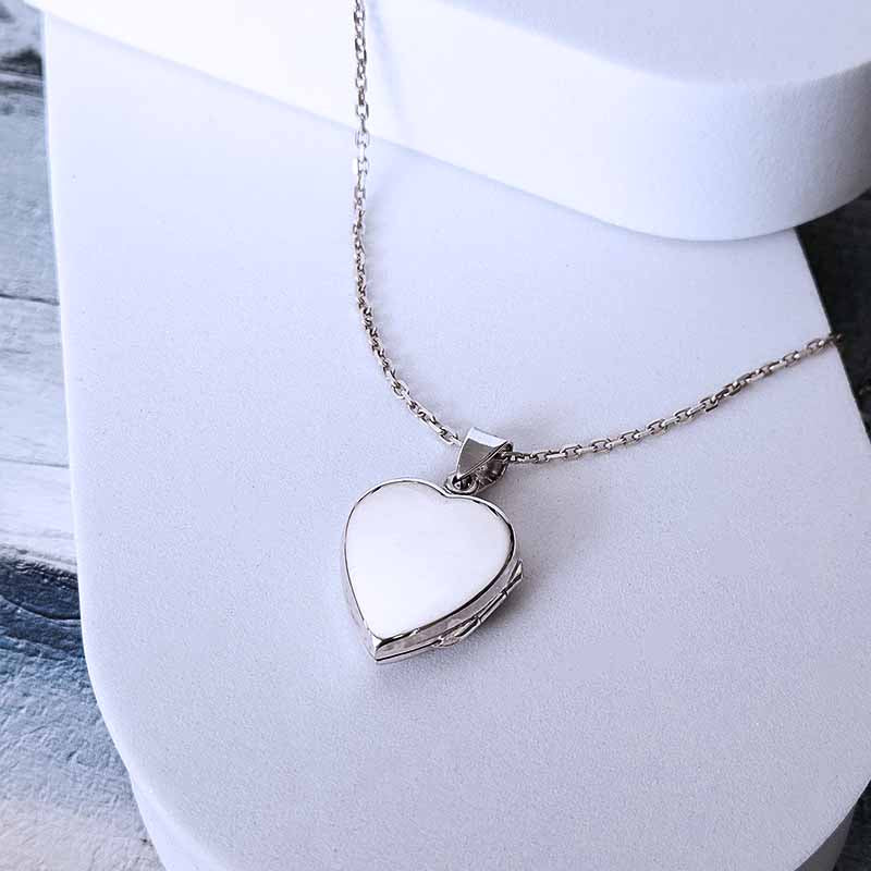 Heart-shaped silver locket on a white stand with a light wooden surface.