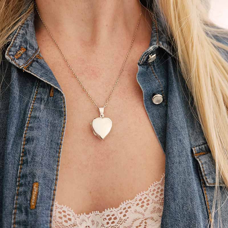 Heart-shaped pendant necklace worn by a person with denim jacket and lace top.
