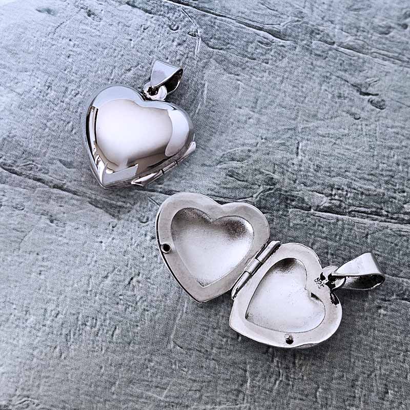 Two silver heart-shaped pendants on a textured gray surface